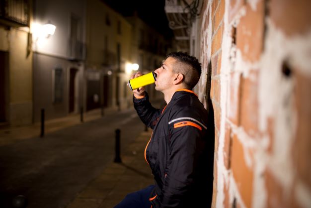 Man leaning against wall drinking liquid energy drink